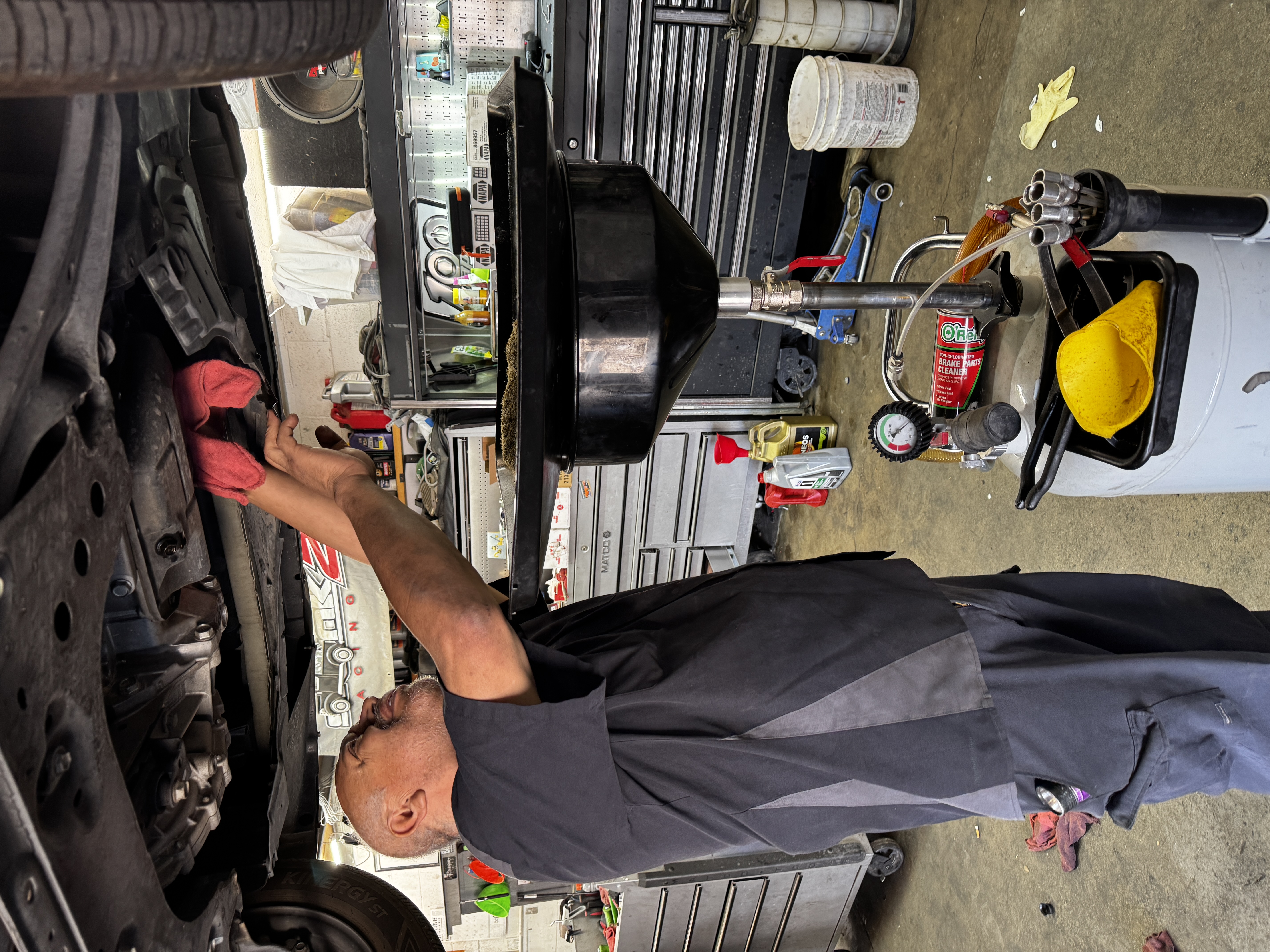 Technician performing oil service under a lifted vehicle